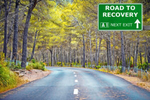 tree-lined road with sign that signs road to recovery